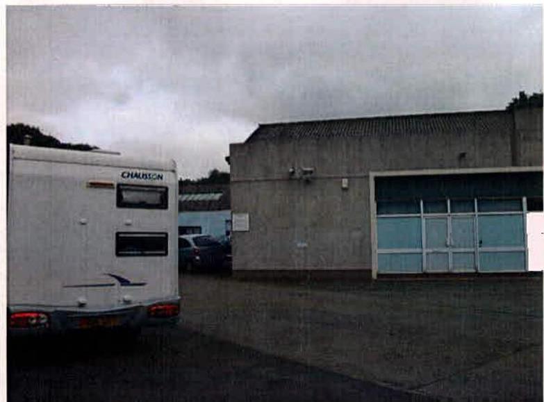 A photograph showing a white caravan parked alongside a concrete building with a large garage-style door.