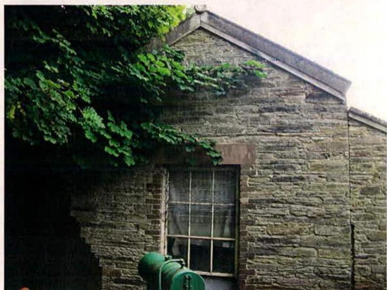 A photograph showing the exterior of a stone building with a window and ivy growing on the wall, likely the laundry building mentioned in the application.