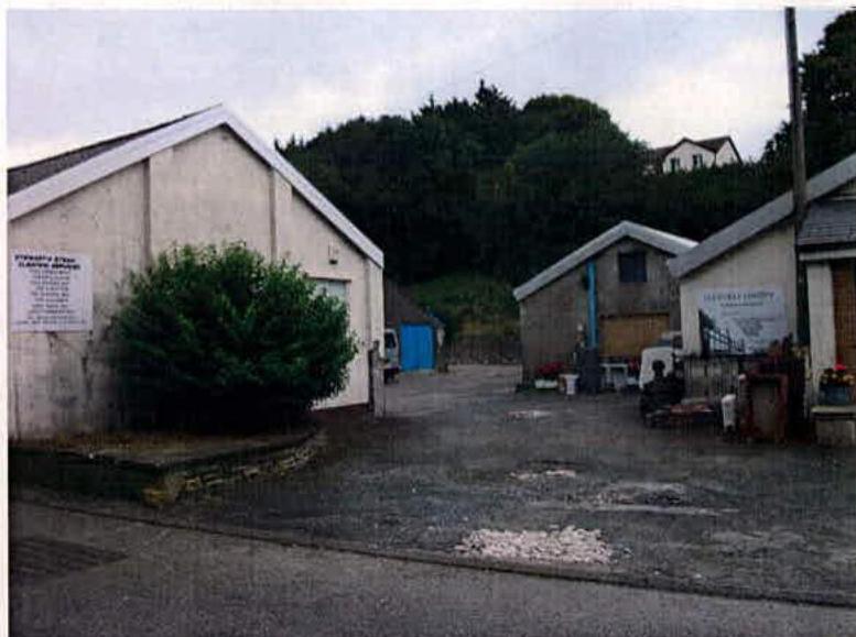 A street-level photograph showing a paved yard with white industrial buildings, including one labeled 'Prestatyn Street Cleaning Services' and another labeled 'Glenfaba Laundry'.