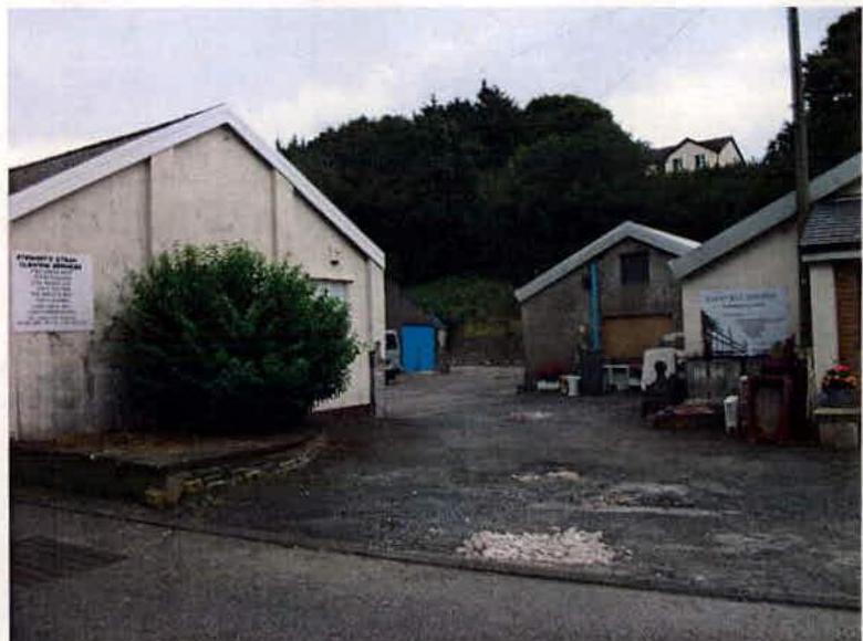 This image shows the exterior of an industrial site featuring white buildings with 'Stewart's Steam Laundry' signage and a paved yard.
