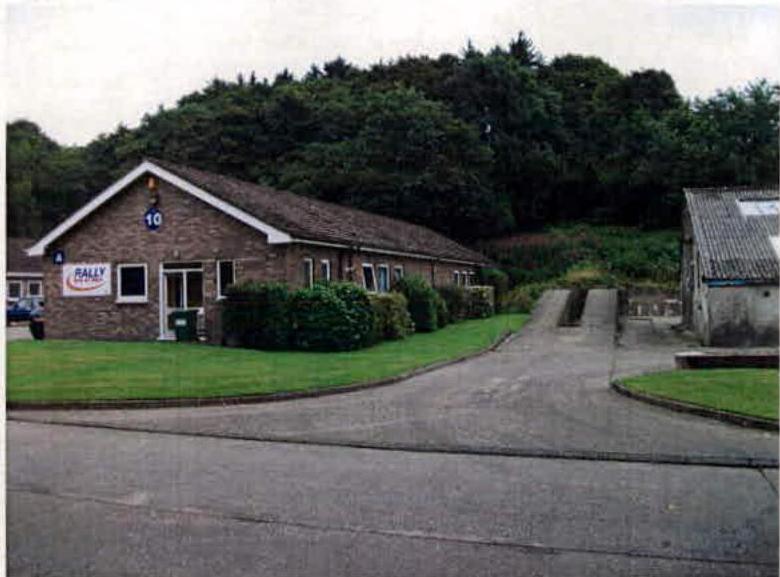 A photograph showing a single-story brick commercial building with a 'RALLY' sign and a paved driveway, alongside a smaller outbuilding to the right.