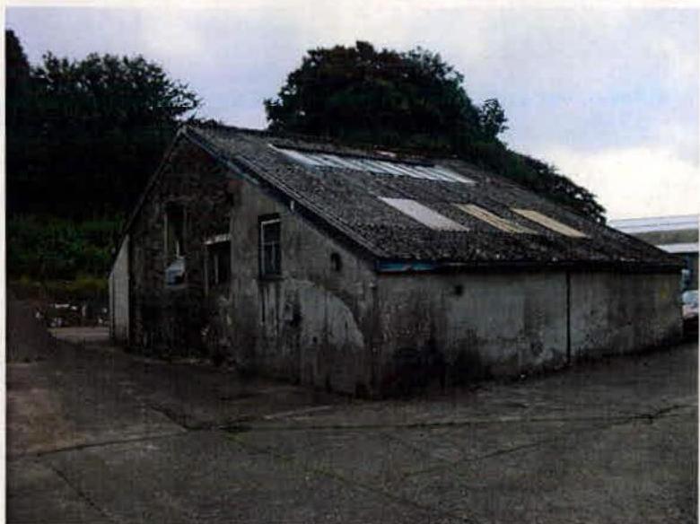 A photograph showing a weathered, single-story industrial building with a slate roof and skylights, appearing to be the structure proposed for demolition.