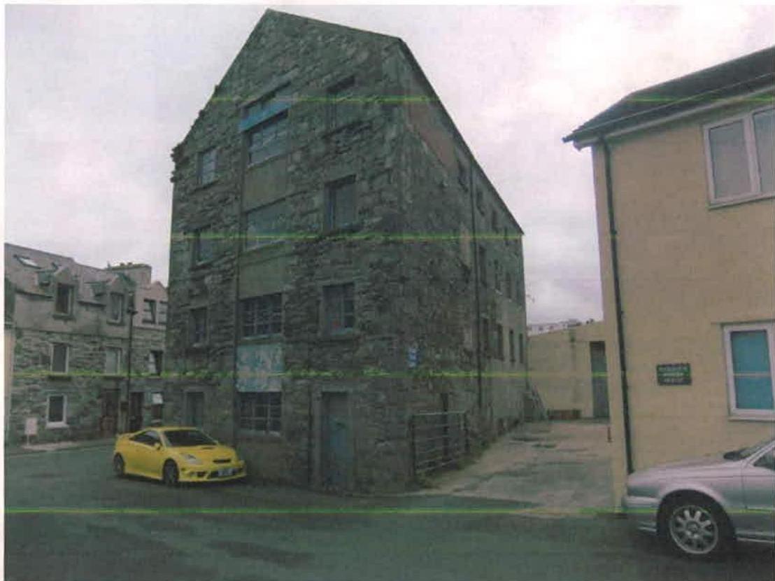 A photograph showing the exterior of a large, multi-story stone warehouse building situated on a street corner, likely the subject of the conversion application.