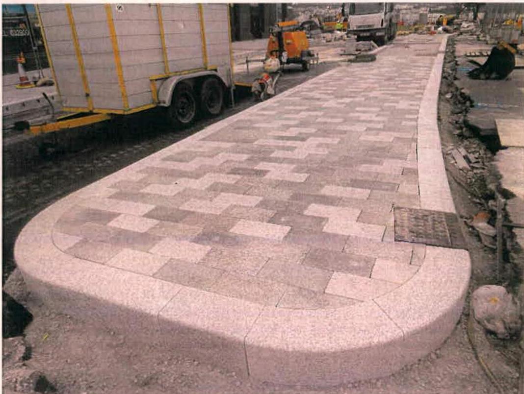 A photograph showing a newly paved section of a promenade with a curved stone edge and construction equipment in the background.