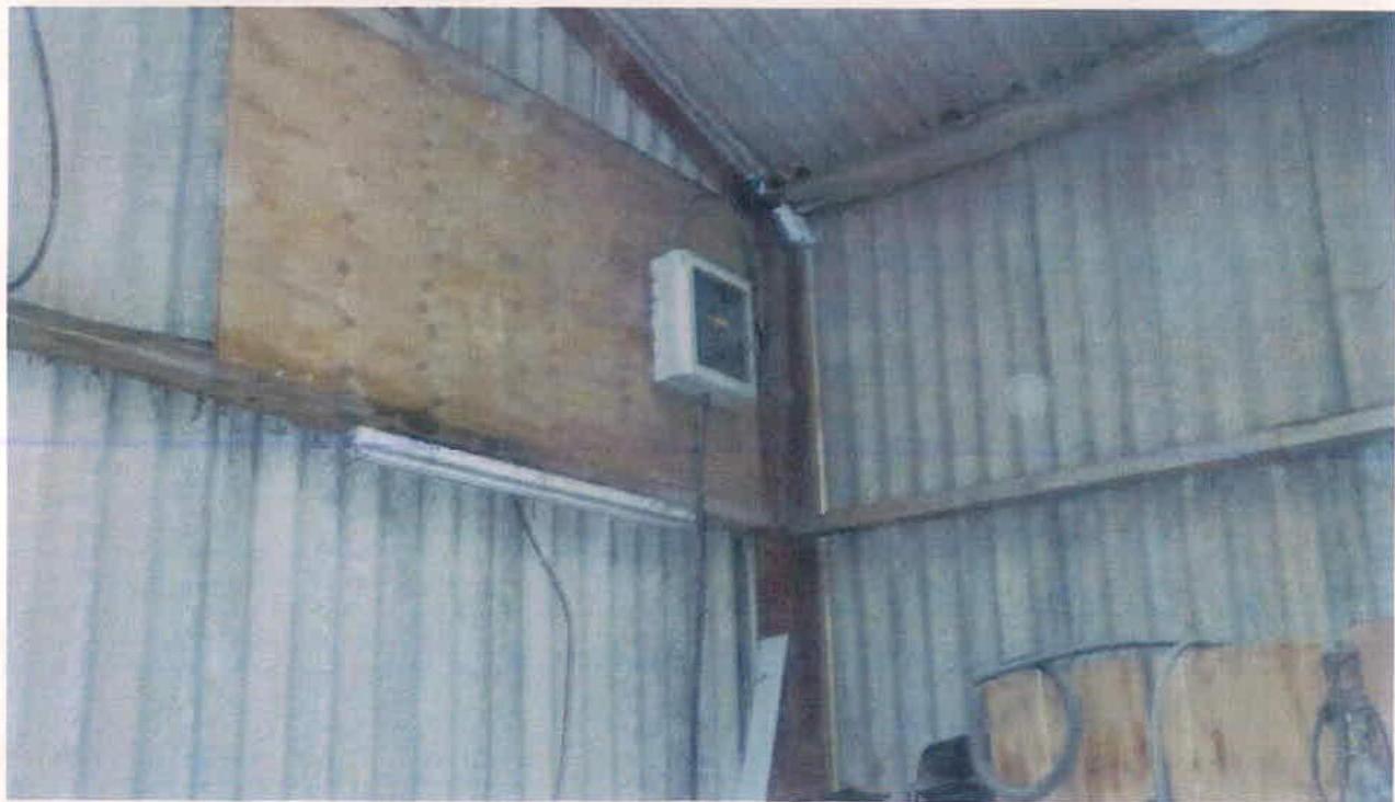 Interior photograph of a corrugated metal outbuilding, likely a shed or barn, showing an electrical control box mounted on a wooden panel.