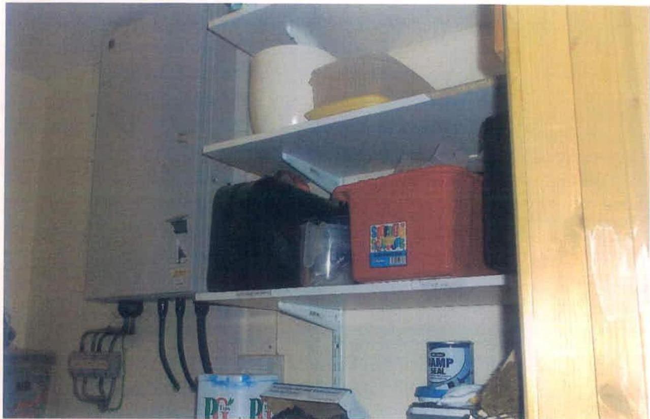 A low-quality photograph showing the interior of a utility cupboard or control unit containing an electrical enclosure on the wall and shelves with storage boxes.