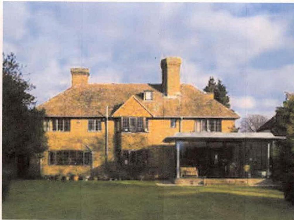 A photograph of a large, two-story detached brick house with a tiled roof and a modern single-story extension attached to the right side.