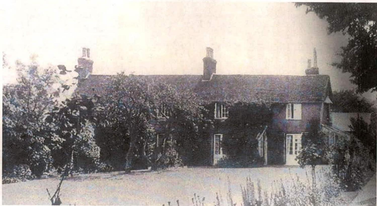 A grainy black and white photograph showing a long, single-story residential building with chimneys, surrounded by trees and a driveway.