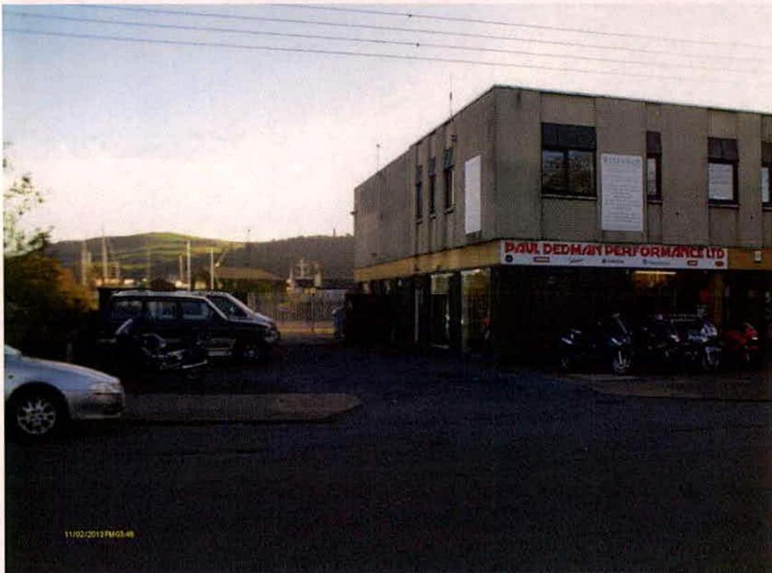 A photograph showing a two-story commercial building with a sign for 'Paul Dedman Performance Ltd' and vehicles parked in the foreground.