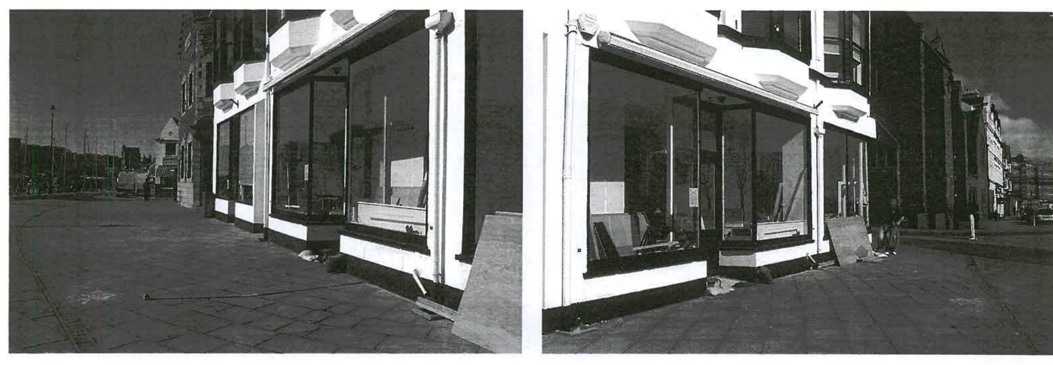 Black and white photograph showing the exterior facade of a commercial building with large windows and a paved area in front.