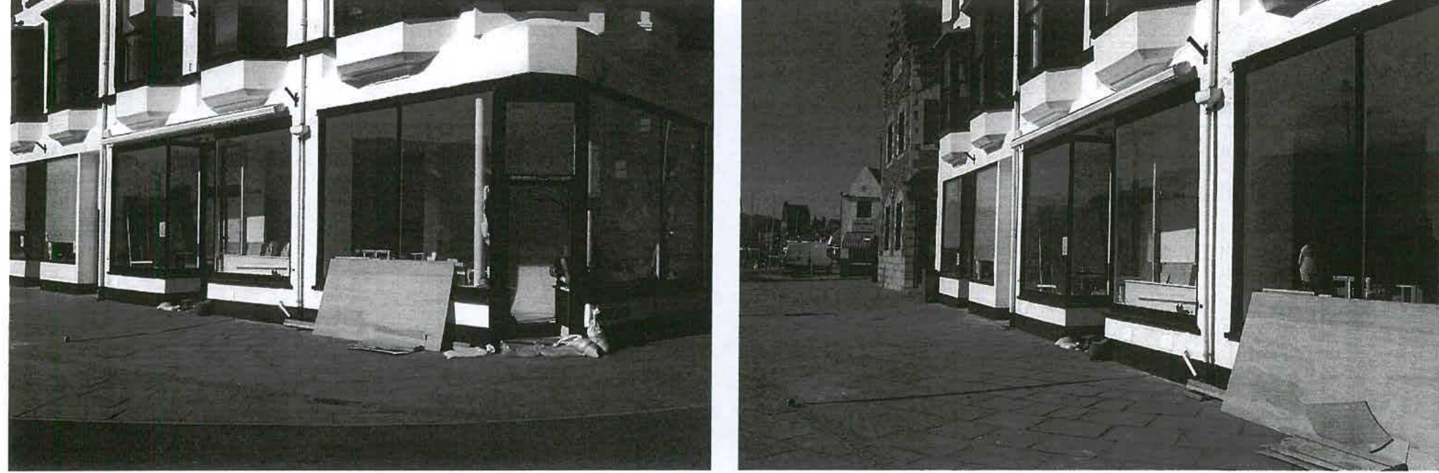 Black and white photograph showing the street-level facade of a commercial building with large glass windows and a paved area in front.