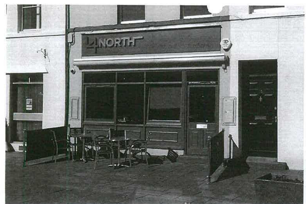 A black and white photograph showing the exterior of a commercial property named 'NORTH' with an existing outdoor seating area on the pavement.