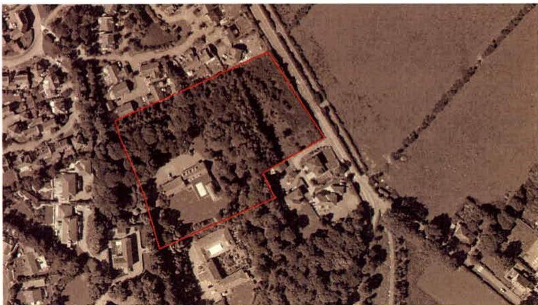 An aerial site plan showing a red-outlined plot of land containing trees and buildings, situated between a residential area and open fields.