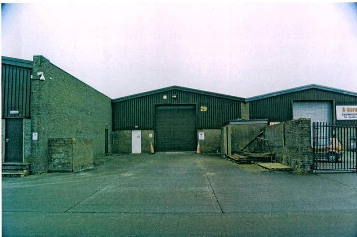 A photograph showing the exterior of an industrial unit with a paved forecourt, roller shutter door, and brick walls.