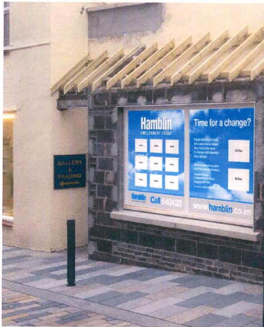 A street-level photograph of a commercial building facade featuring a large window display for Hamblin Employment Group and a wooden slatted awning above it.