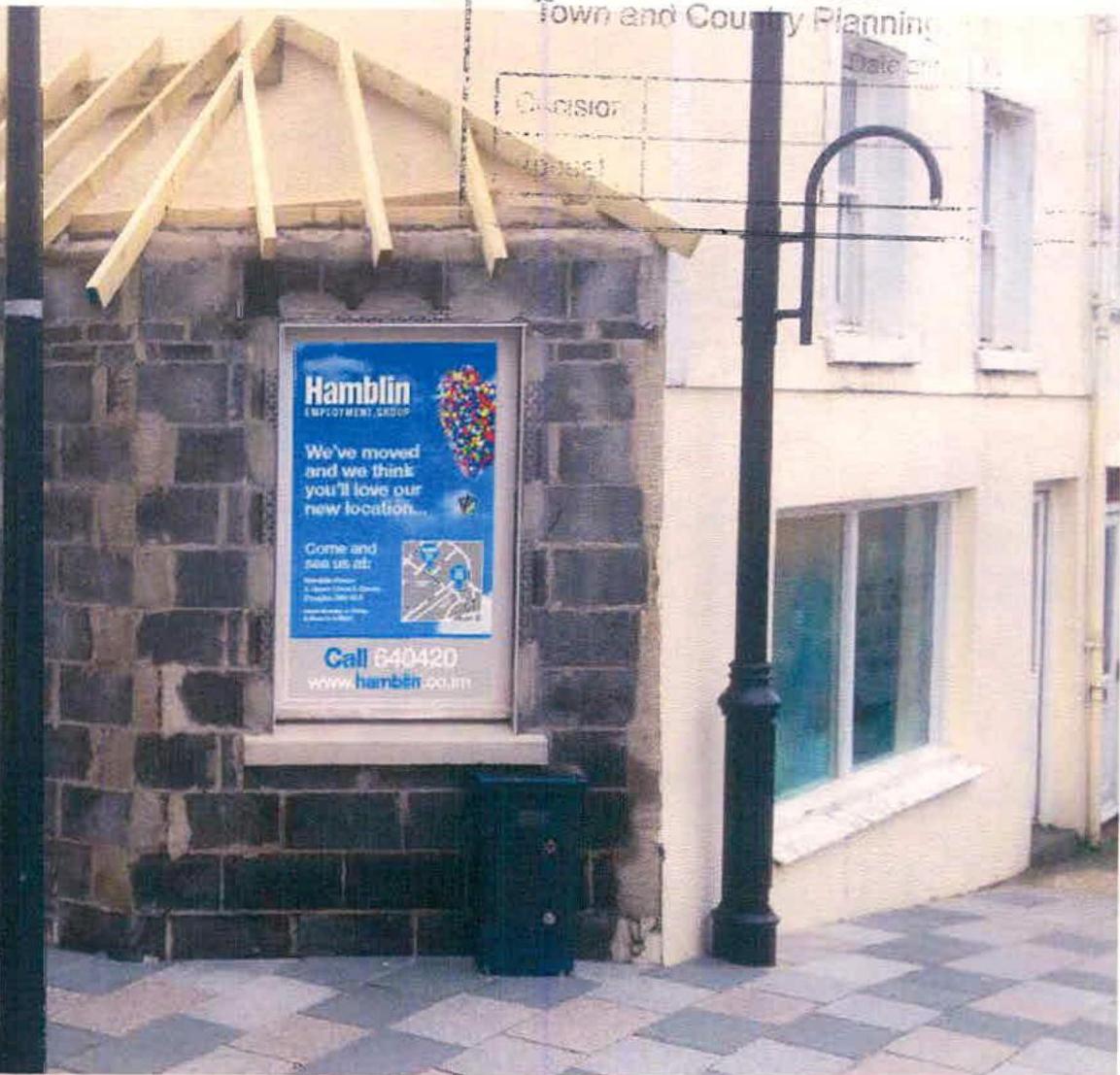 A street-level photograph showing a stone wall corner with a large 'Hamblin Employment Group' window sign and a wooden canopy frame above it.