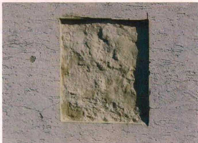 A close-up photograph showing a square patch of rough render or stone on a textured wall surface, likely a material sample or repair detail.