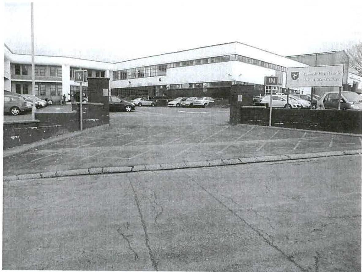 A black and white photograph showing the main entrance, boundary walls, and parking area of a college building.