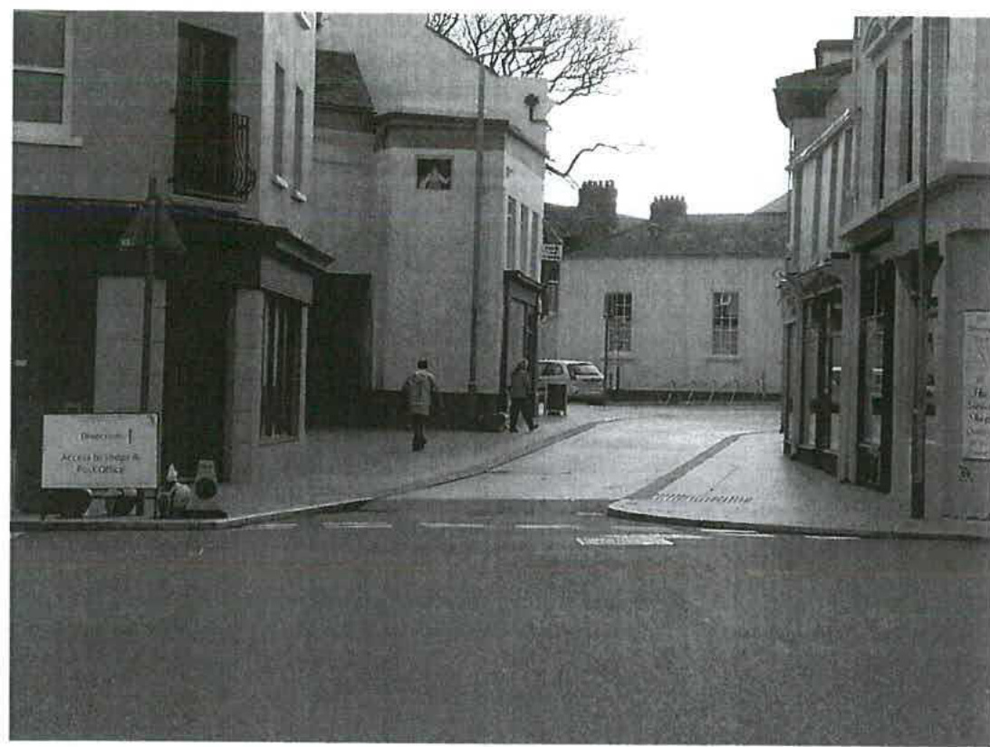 A black and white photograph showing a street scene in Ramsey with buildings on either side, including a sign for the Police Office and pedestrians walking on the pavement.