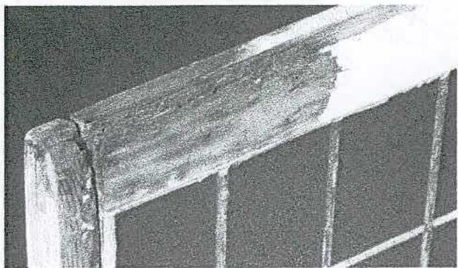 A grainy black and white close-up photograph of a damaged wooden window frame corner, highlighting a split in the timber.