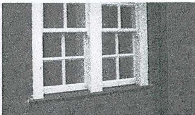 A close-up photograph of a white, multi-paned window set into a dark wall, illustrating the existing window works mentioned in the application.