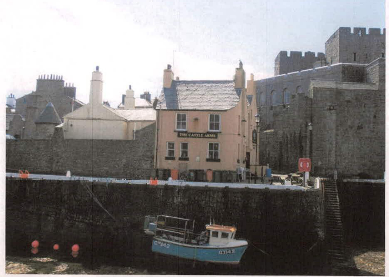 A photograph showing a harbor scene featuring 'The Castle Arms' pub and a large stone castle wall in the background with a small boat in the foreground.