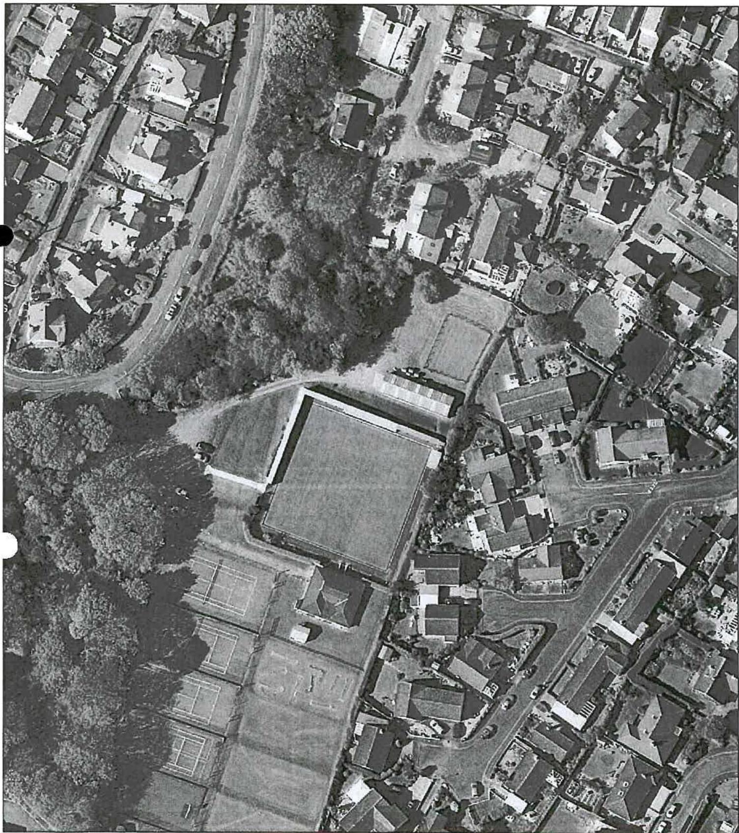 Black and white aerial photograph showing a residential area with a large sports facility and tennis courts.