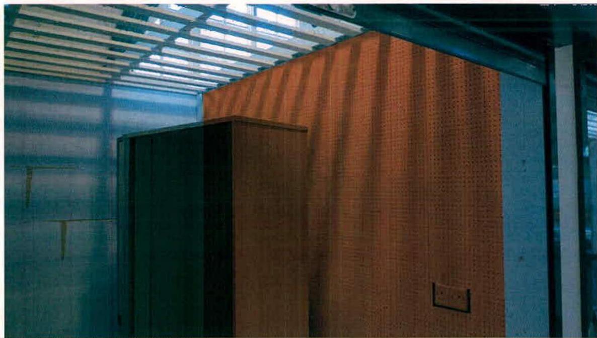 An interior photograph showing a large wooden partition or wall panel with a perforated texture beneath a slatted ceiling structure.