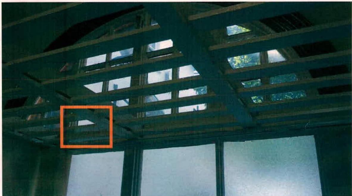 An interior photograph looking up at an exposed wooden timber roof structure with gaps, featuring an orange box highlighting a specific beam.