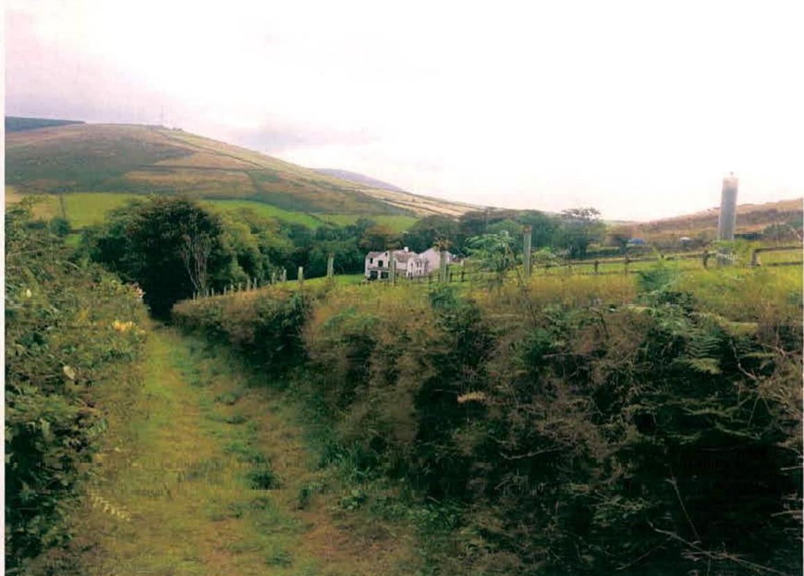 A photograph showing a rural landscape with a white detached house situated in a green valley, surrounded by hills and vegetation.