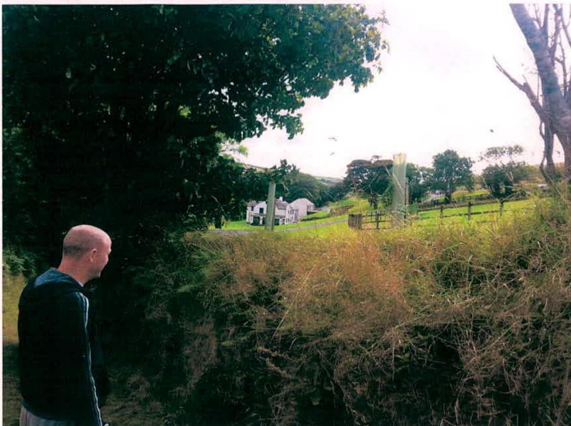 A photograph showing a man in the foreground looking towards a white detached house situated in a rural landscape with trees and fields.