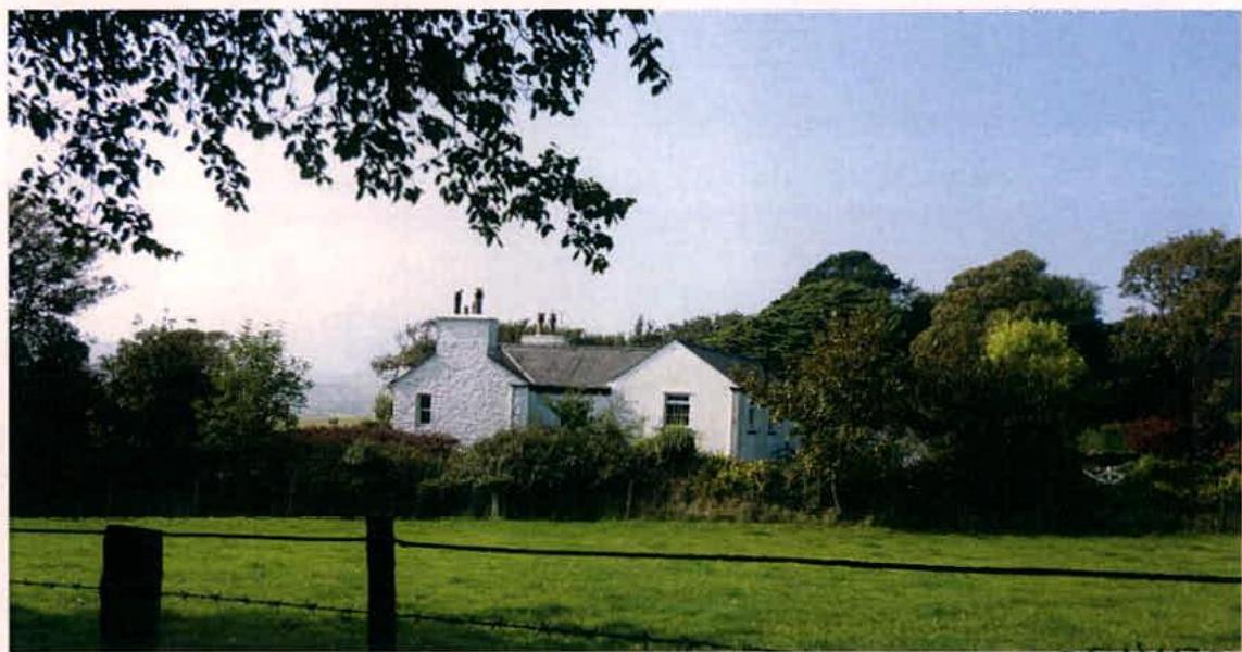 A photograph showing a white detached house situated in a rural landscape with green fields and trees.