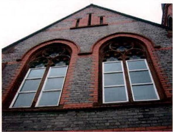 A low-angle photograph showing the upper brick facade of a building with two large arched windows featuring decorative tracery.