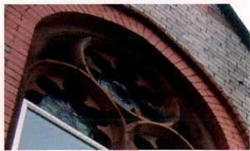 A close-up photograph showing a red brick arched opening with intricate internal detailing and a modern window frame at the bottom.