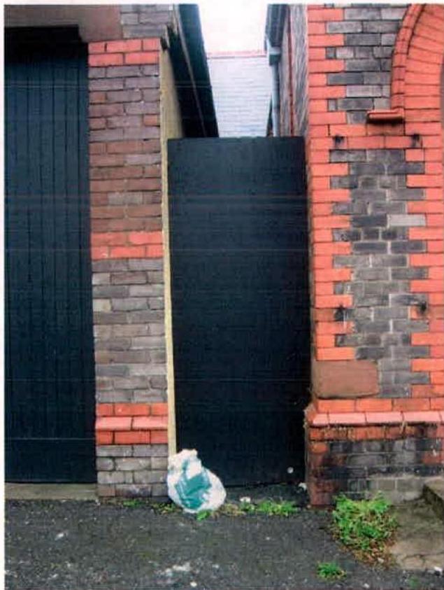 A photograph showing a black gate and brick boundary wall with an arched feature.