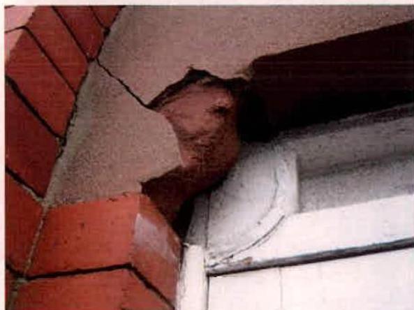 A close-up photograph showing significant structural damage, specifically a large crack running through the rendered wall and brickwork at the corner of a building near a window frame.