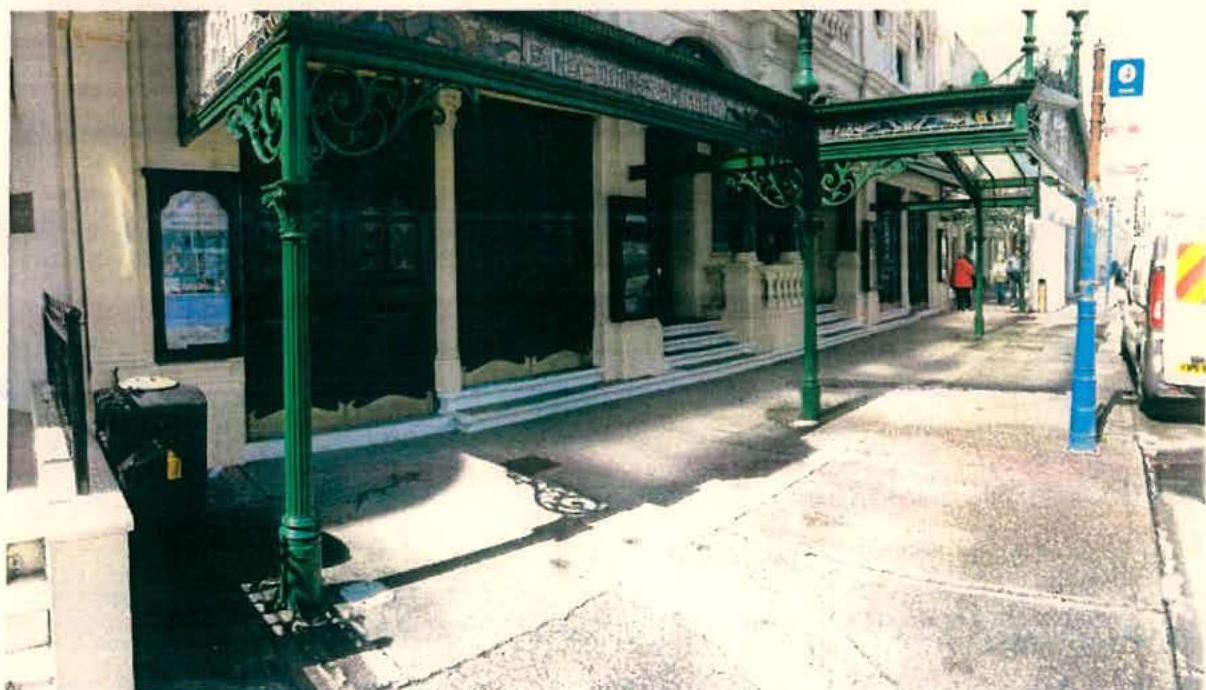 A photograph showing the exterior of a building featuring a distinctive green metal canopy extending over the footway.