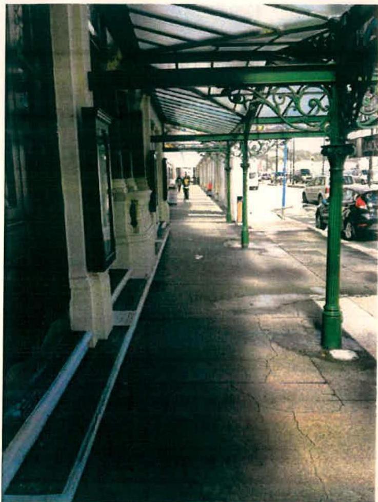 A photograph showing a historic covered footway with distinctive green cast-iron pillars and a canopy structure alongside a building.