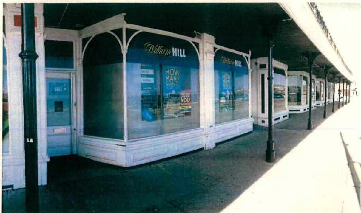 A photograph depicting a row of white Victorian-style kiosks along a covered promenade, featuring a William Hill betting shop.