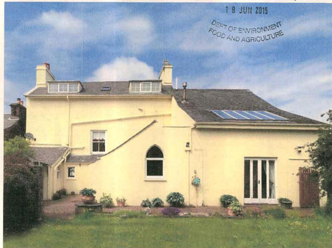 A photograph showing the exterior of a yellow, two-story detached building with a slate roof, dormer windows, and solar panels.