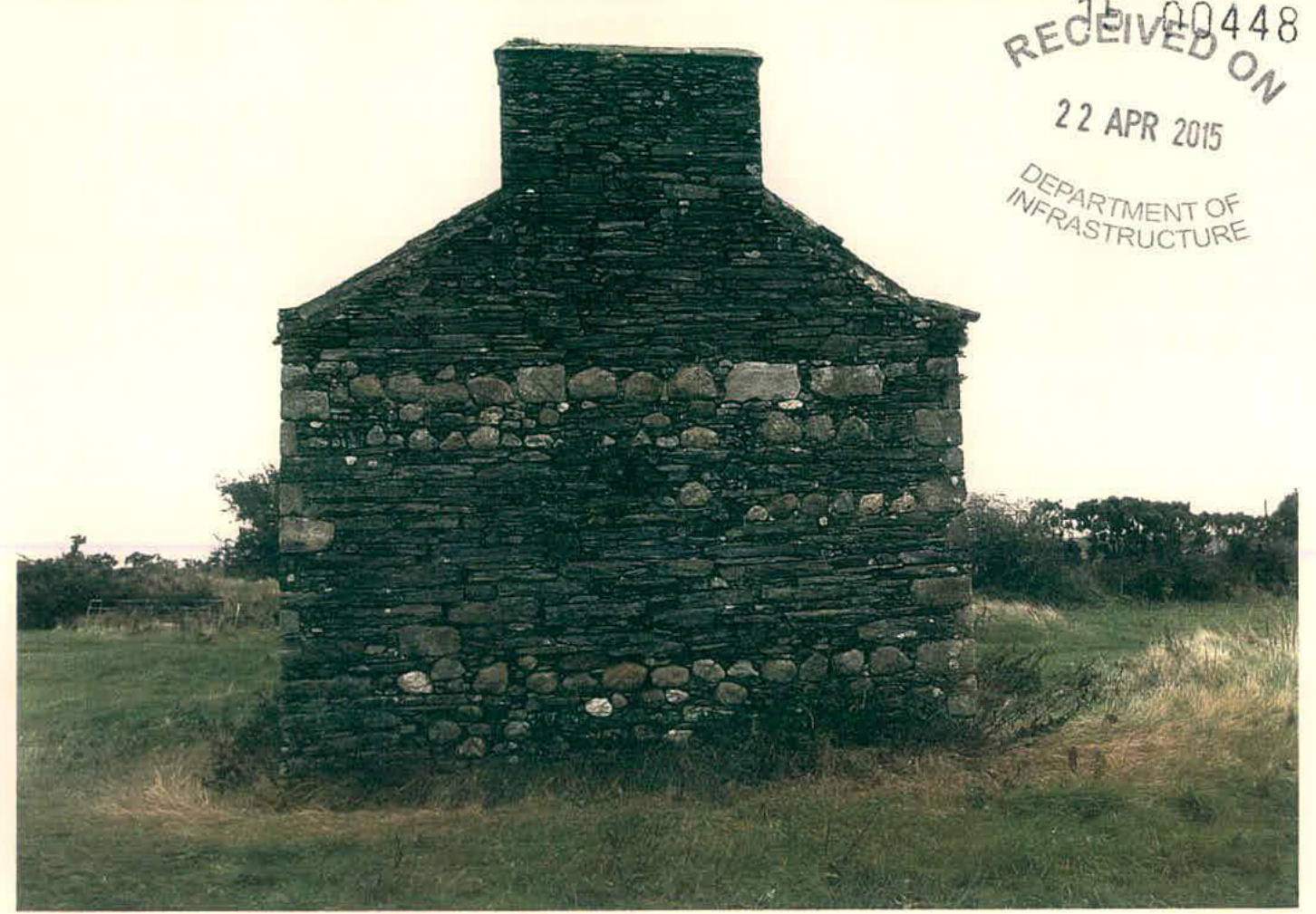 A photograph showing the rear elevation of an existing stone tholtan cottage situated in a grassy rural field.