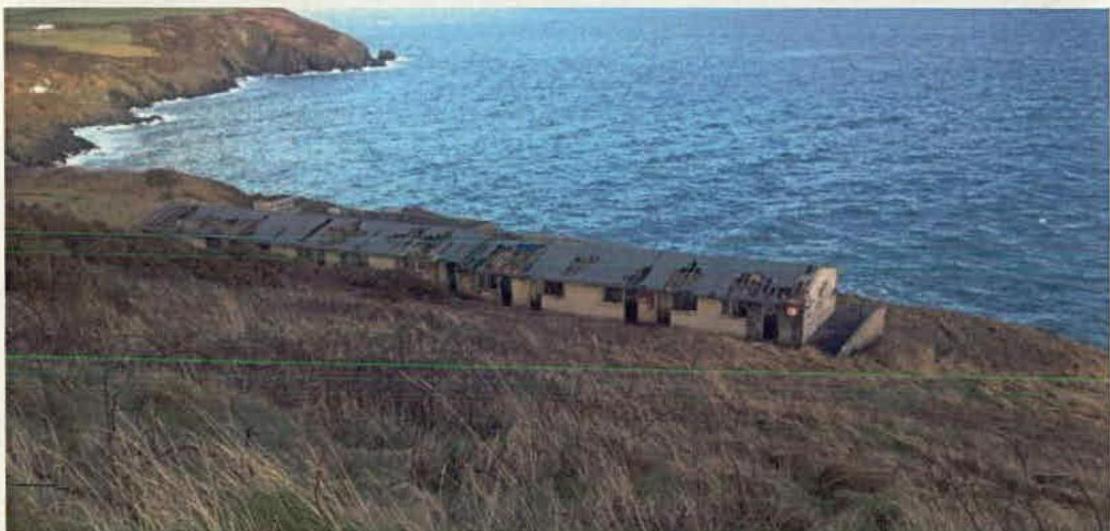 A photograph showing a long, low building situated on a grassy cliff edge overlooking the ocean.