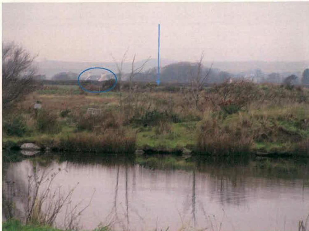 A landscape photograph showing a rural field with a stream in the foreground and a white building circled in the distance. Blue annotations highlight specific areas of the site.