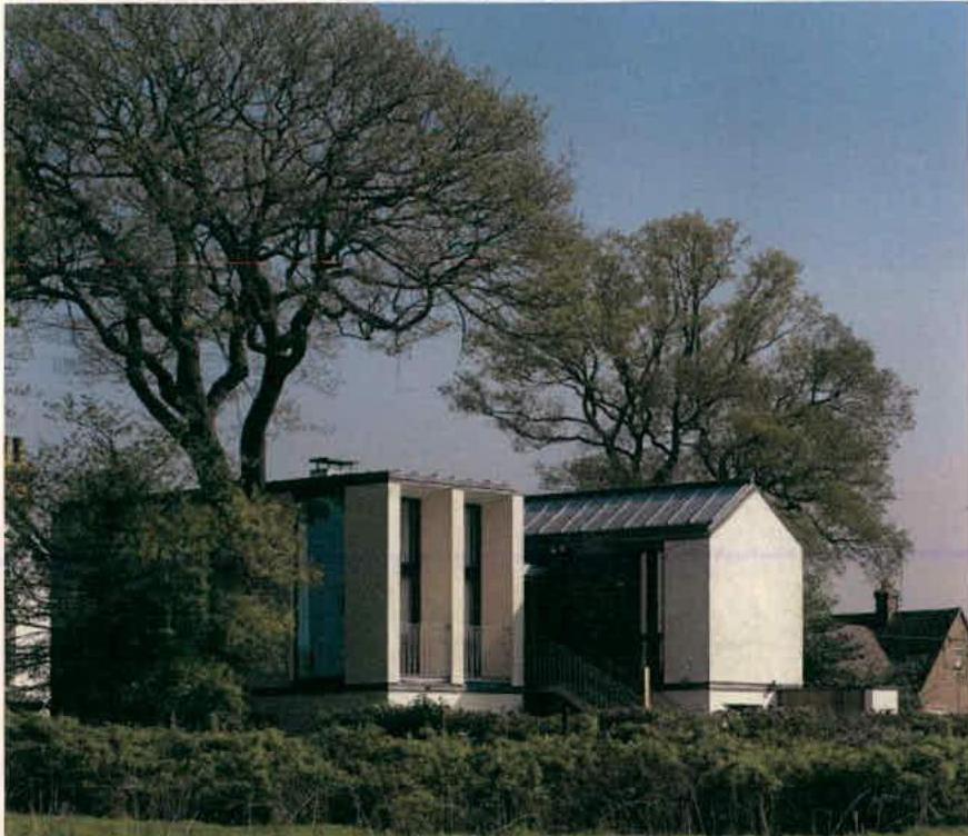 A photograph of a modern detached dwelling with mixed roof styles, surrounded by large trees and vegetation.