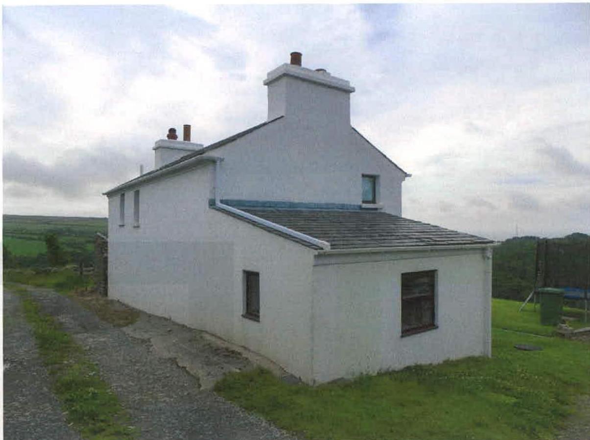 A photograph of a white detached house with a slate roof and chimneys, situated in a rural setting with a gravel driveway.