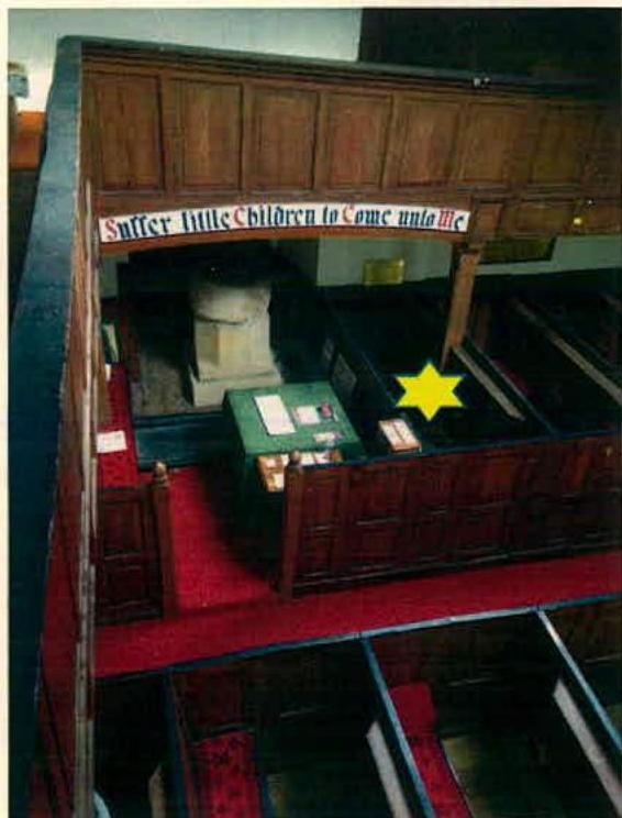 This photograph shows the interior of a historic church or chapel with wooden pews, red carpeting, and a banner reading 'Suffer little Children to Come unto Me'. A yellow star highlights a specific area, likely indica...