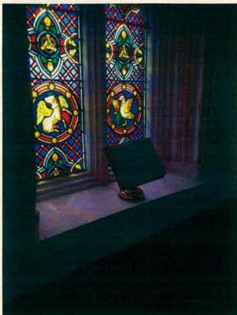 A photograph showing a detailed view of a stained glass window with colorful geometric patterns and figures inside a dimly lit room.