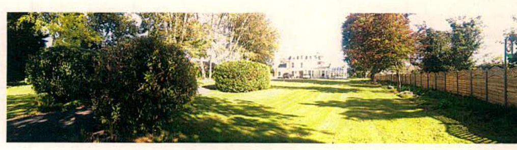 A panoramic photograph showing a grassy garden area with mature trees and a wooden fence, with a white detached house visible in the background.