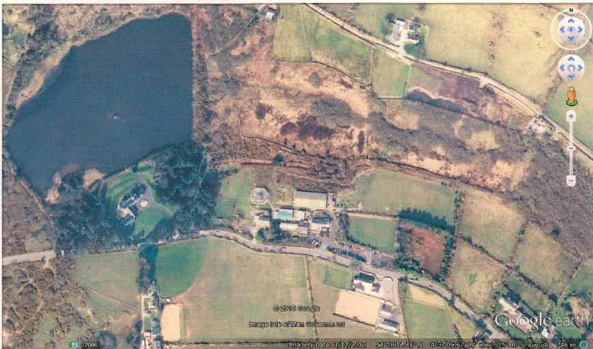 Aerial satellite view showing a rural site with a large lake, fields, and existing buildings.