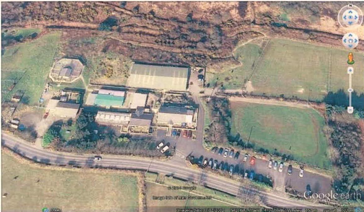 Google Earth aerial screenshot showing a rural site with a large building complex, parking lot, and surrounding fields.